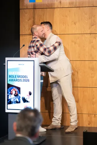 Nils Binder umarmt auf der Bühne Moderator Pavlo Stroblja, der ihm den Queermentor Role Model Award überreicht.