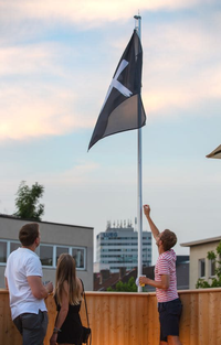 Three people look from below at a hoisted flag, on which the 9elements logo can be seen.