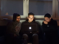 Three people sitting on a couch in the dark and coding together